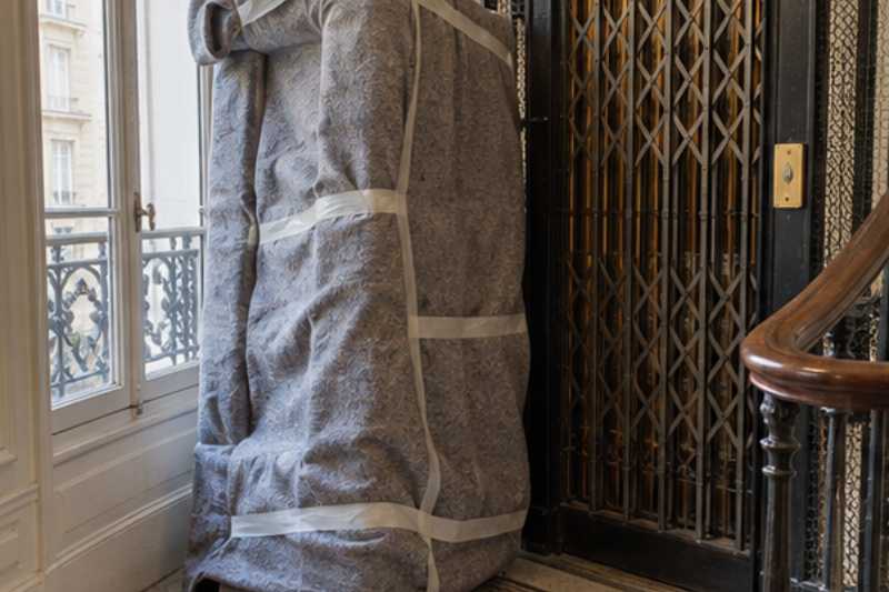 Canapé sous couverture sur un palier, à côté d'un petit ascenseur ancien, le canapé a pris l'escalier