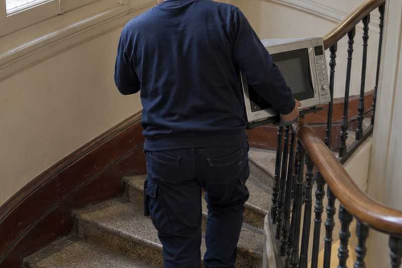 Déménageur descendant un escalier avec un four à micro-ondes, l'électroménager ne tenait pas dans l'ascenseur